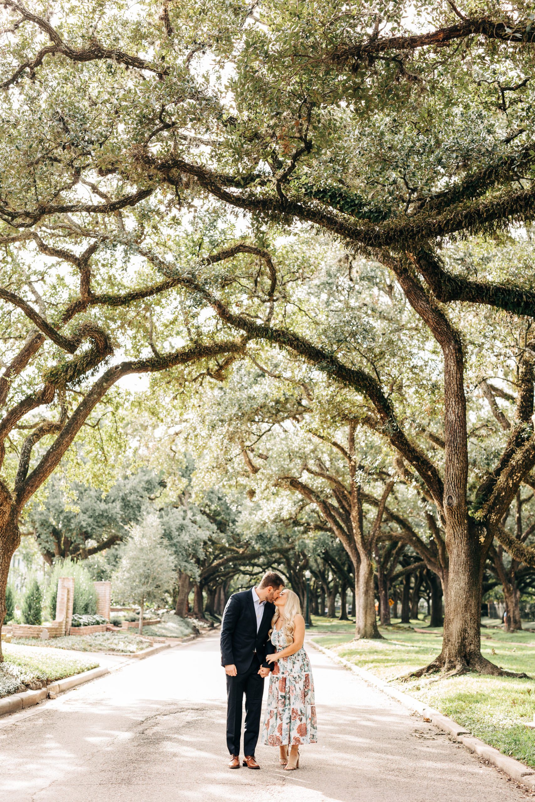 couple walking through large oak trees during engagement session