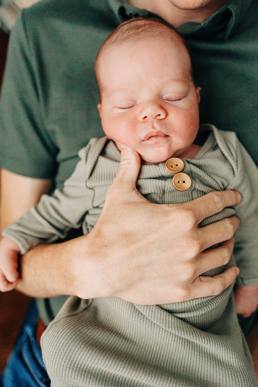 A newborn baby boy sleeps on dad's chest in a green onesie houston doulas