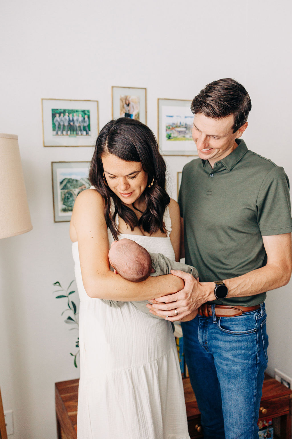 A mom holds her sleeping newborn baby in her arms while dad places a hand on the baby