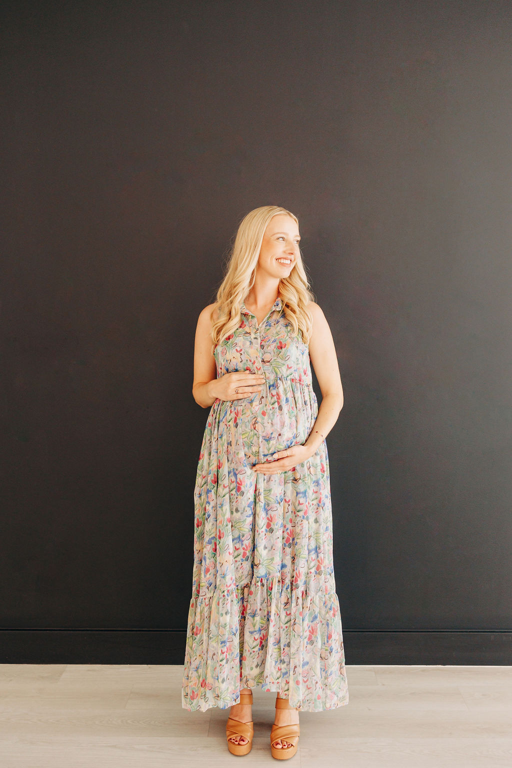 A mom to be looks over her shoulder in a colorful maternity dress in a studio