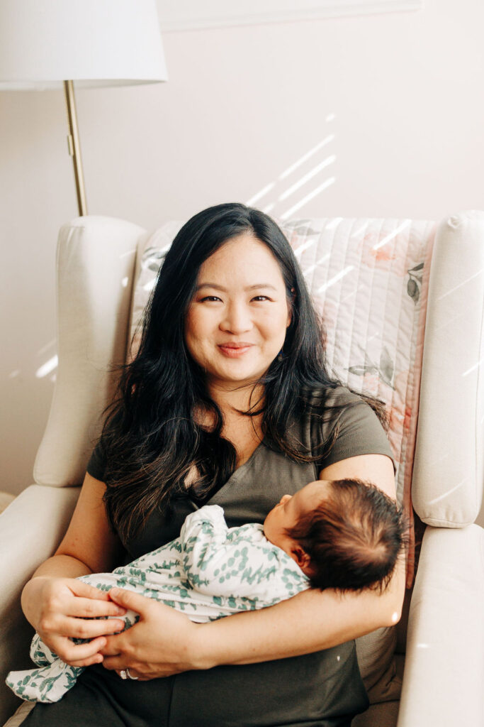 A new mom sits in a nursery chair while holding her sleeping newborn baby
