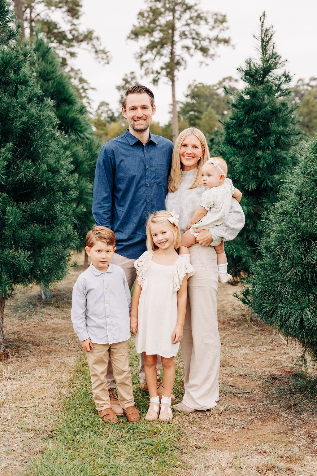 A mother stands in a houston christmas tree farms carrying her infant daughter with her husband and two toddler children