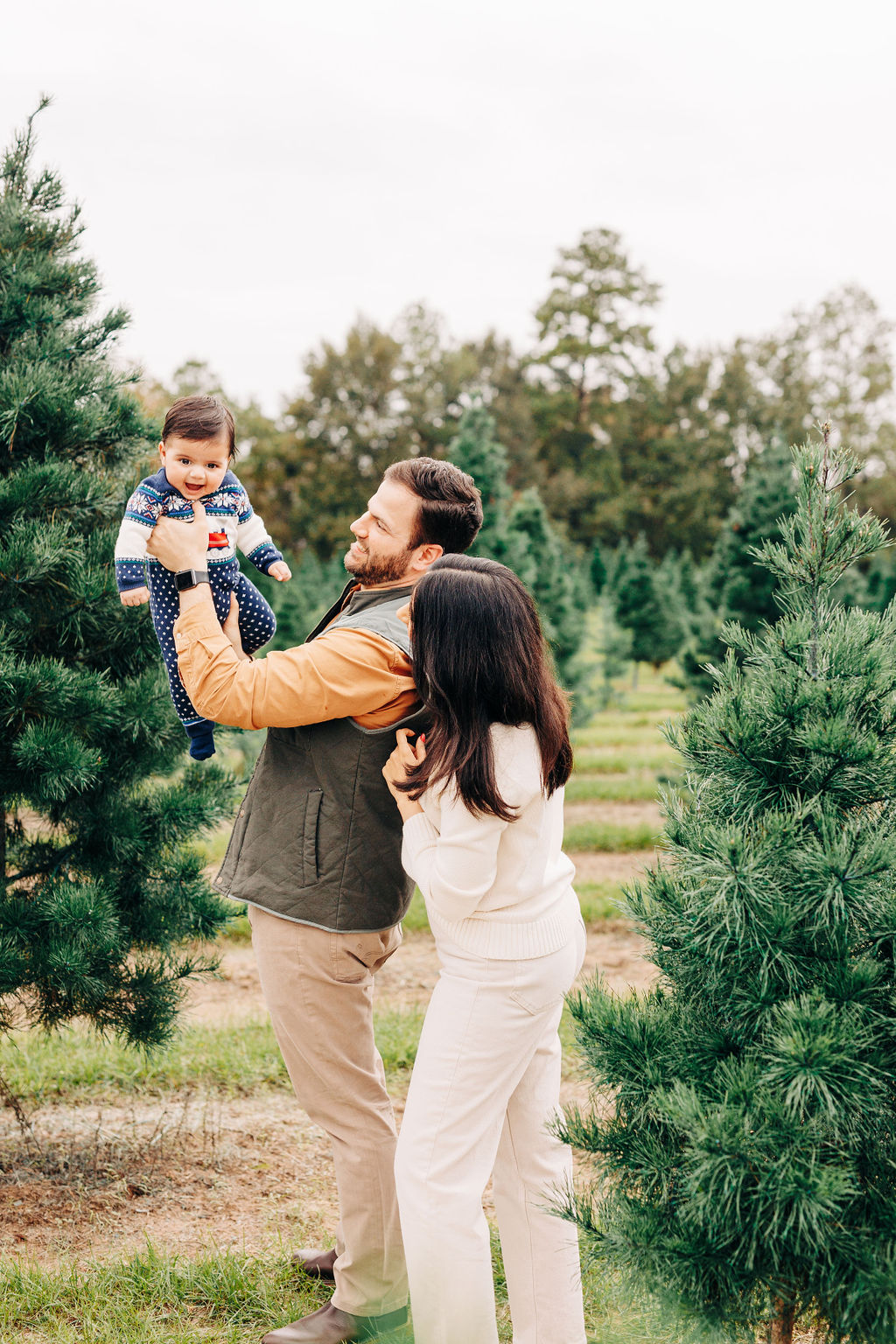 Happy parents lift and play with their toddler baby in a sweater onesie