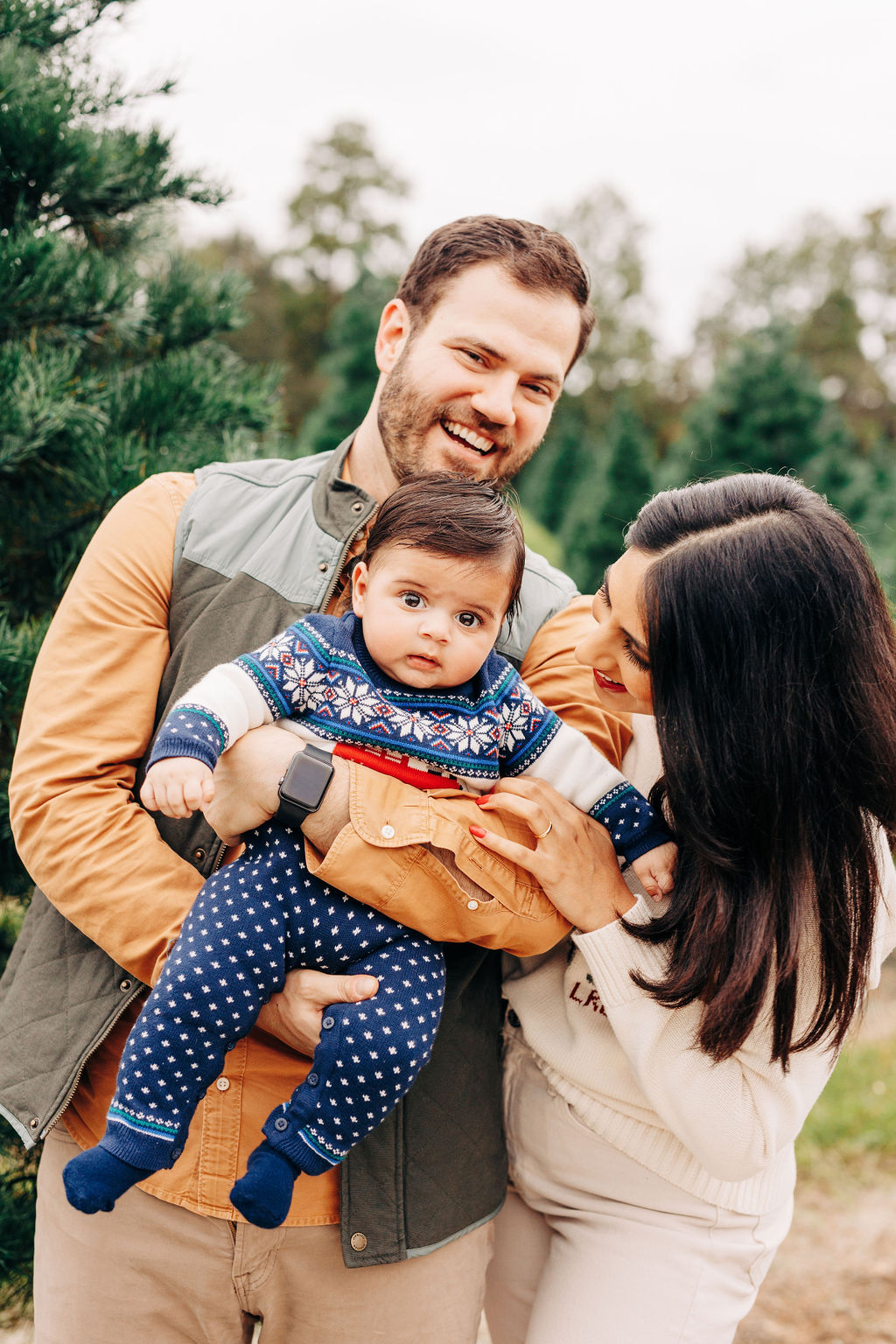 A scared looking toddler in a colorful onesie sits in dad's arms while mom leans in while standing outside