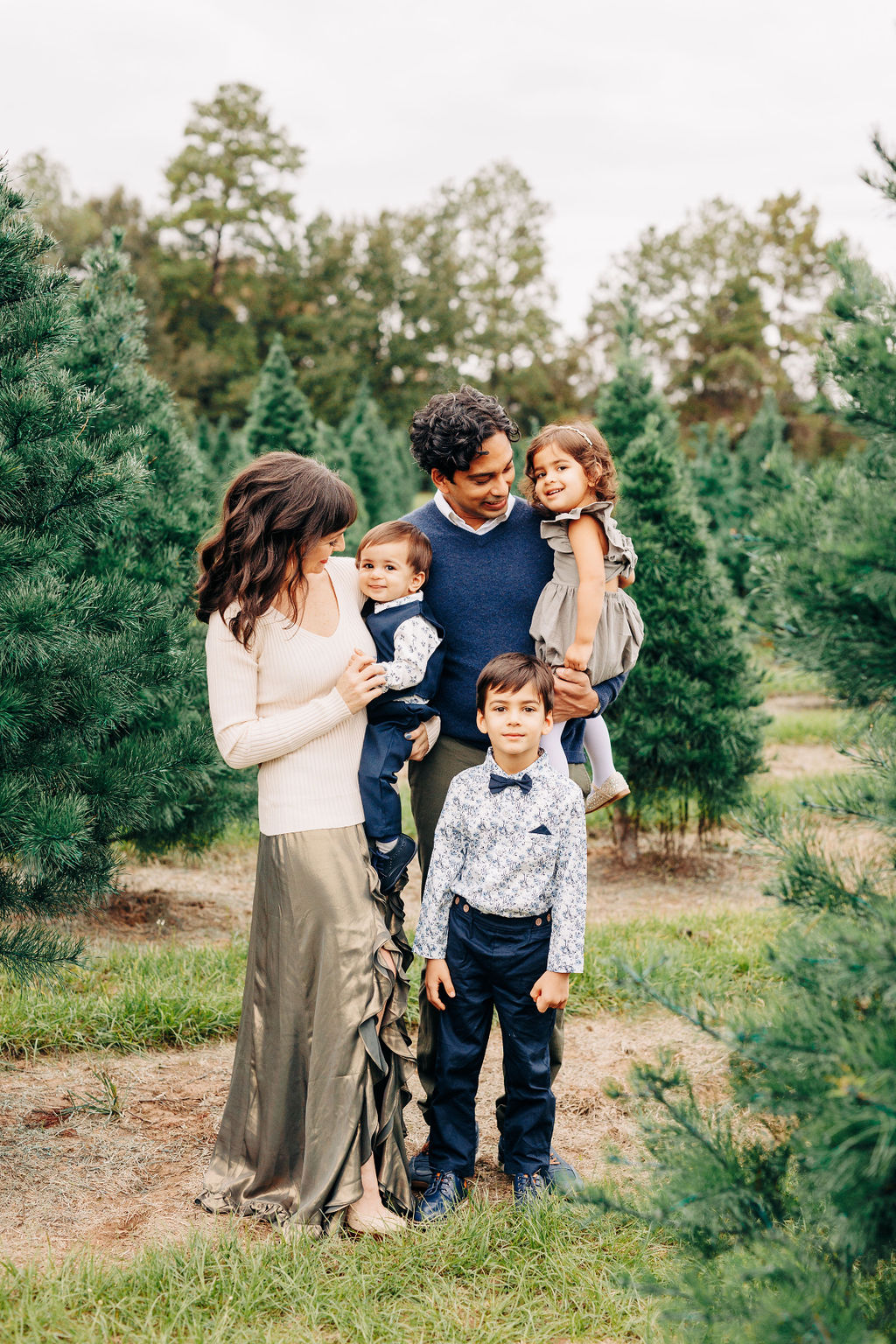 A mother and father play and laugh with their three young children in houston christmas tree farms