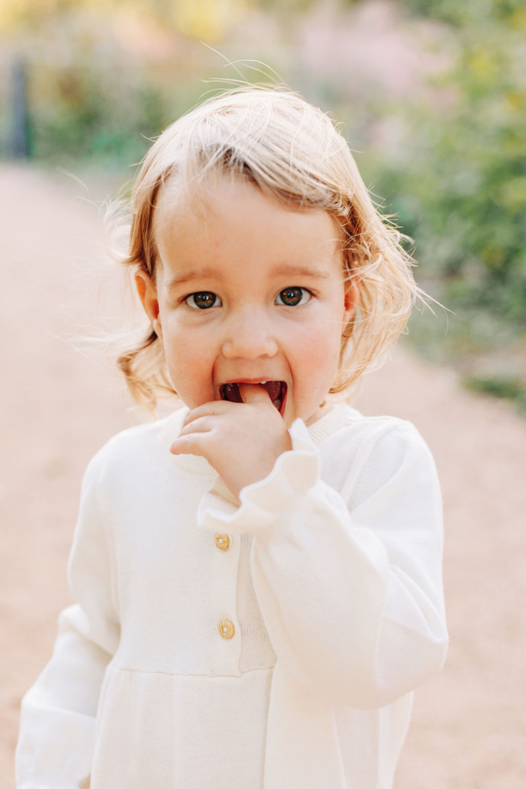 A young toddler girl stands in a park path with a finger in her open mouth during things to do in houston with toddlers